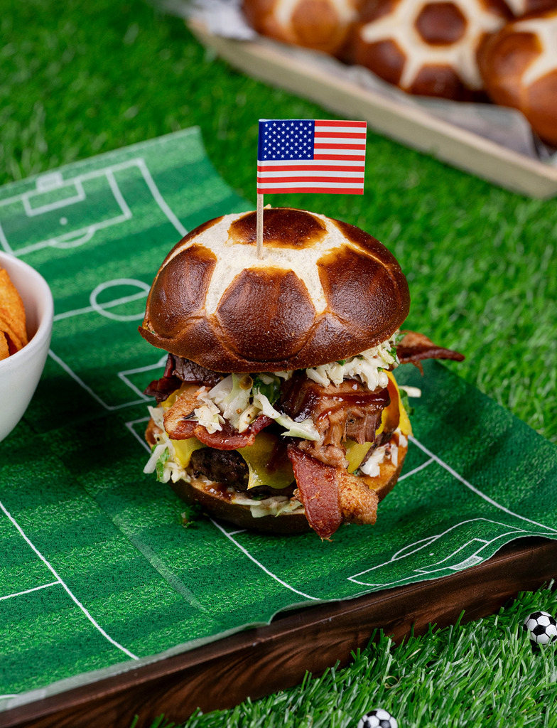 BBQ brisket burger with bacon, American cheese, coleslaw and pickles on a pretzel soccer bun